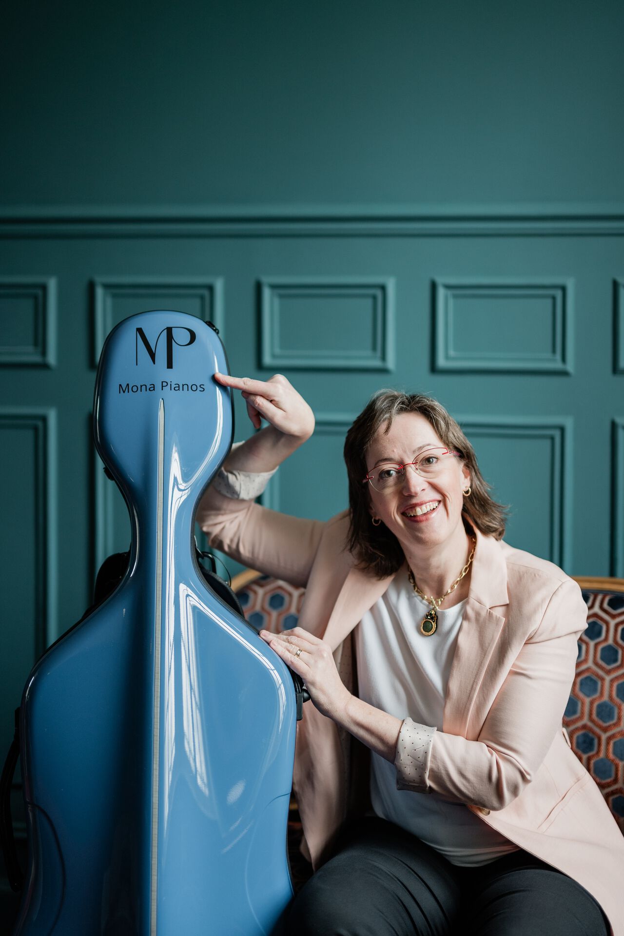 Mona Parmentier désignant le logo Mona Pianos sur son étui de violoncelle